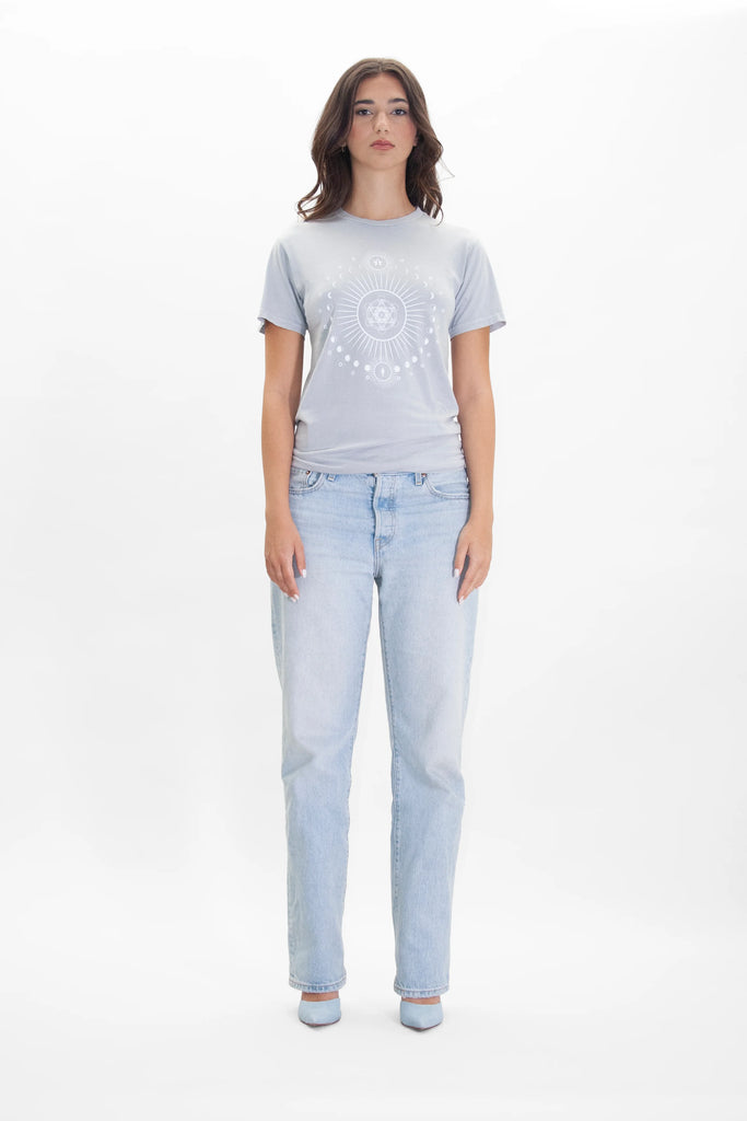 Woman standing against a white background, wearing a GFLApparel Moon Metatron Tee in Galactic Gray and light blue jeans, with hands resting by her sides.